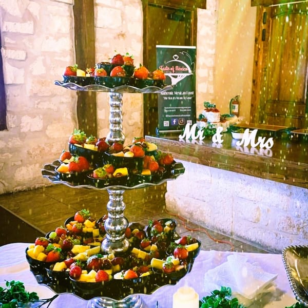 A three-tiered fruit display with strawberries, grapes, and pineapple, with a "Taste of Mexico" sign in the background.